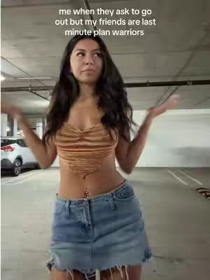 A woman stands in a parking garage with her arms out, wearing a crop top and denim skirt. Text overlays the image.