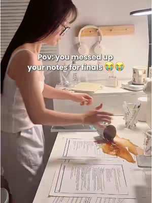 A person is spilling a dark liquid, likely coffee, onto a desk surface, with papers and a laptop present.