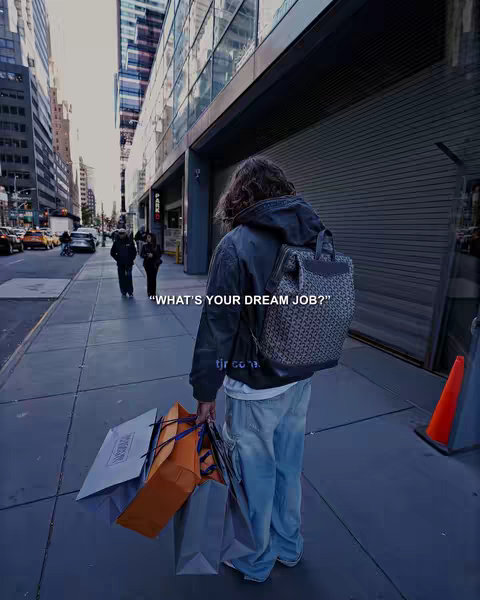 A person walking down a city sidewalk, carrying shopping bags and wearing casual clothes. The scene is captured from a low angle, with the person's back to the camera.