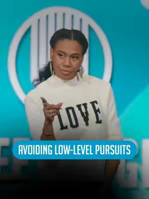 A woman in a white sweater with the word "LOVE" in black letters is addressing the camera with a serious expression. In the background is an abstract teal design and a blurred logo. Below the woman, a rectangular blue box reads, 'AVOIDING LOW-LEVEL PURSUITS'.