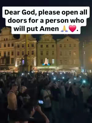A crowd of people is gathered in a plaza at night, with several buildings in the background. The sky is dark. Above the crowd, an image of praying hands with a blue hue and an open heart is seen. Text overlayed on the top part of the image conveys a prayer request. The overall composition suggests a spiritual or community gathering at dusk.