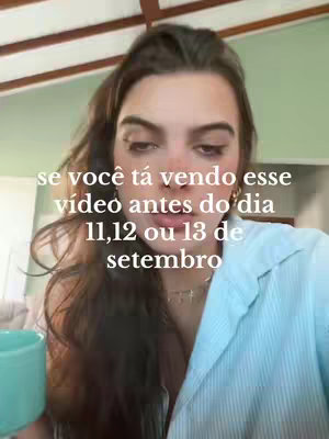 A young woman with long brown hair is inside. She is wearing a light blue button-down shirt. She has dark eyebrows and is looking directly at the camera. Text appears on the video, in white font, explaining that you can watch the video before the days of a specified date set.