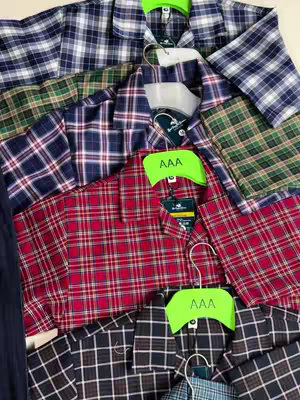An overhead shot of several folded plaid shirts of different colors. The shirts are neatly arranged, with some hanging on hangers. The colors range from blue and white, red and black, green and dark blue, and black and brown.  Each shirt has a tag with the characters "AAA" on it.