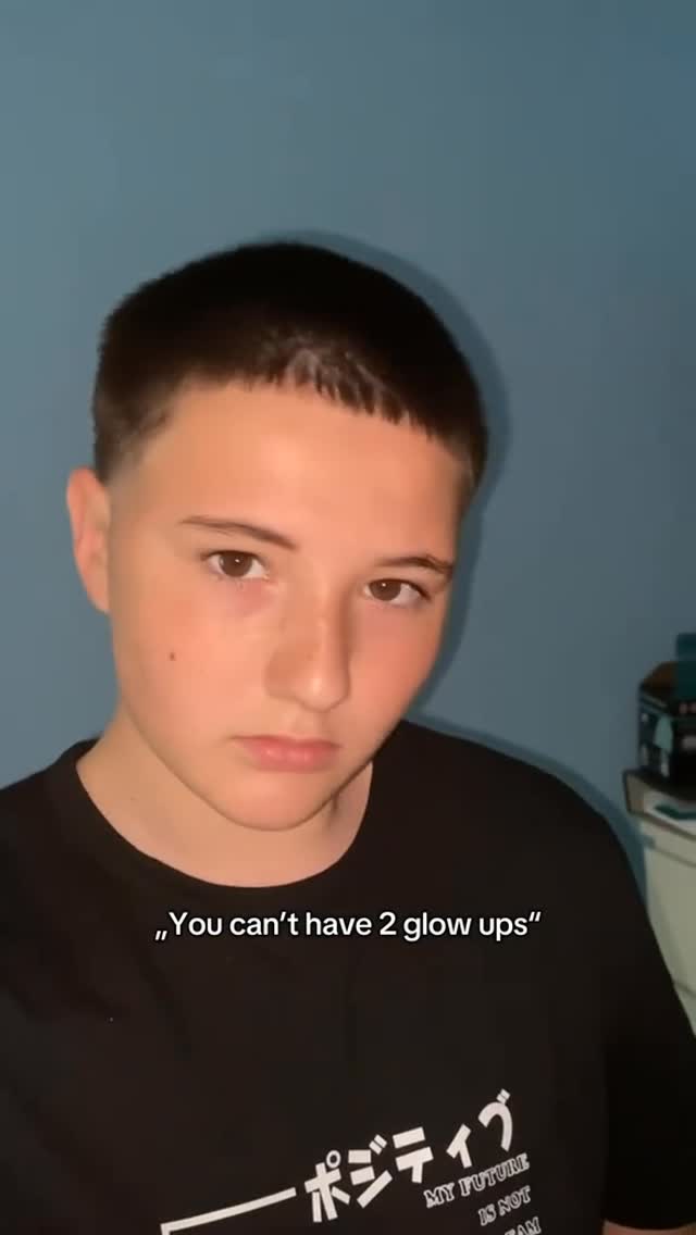 A young person with short hair in a black t-shirt is centered in the frame against a plain blue background. Overlayed text is in a white font at the bottom.