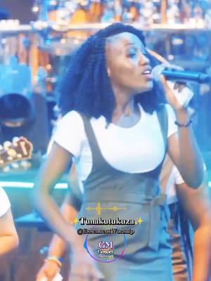 The cover image features a woman with braided hair singing into a microphone. The background is blurred, suggesting a stage or performance setting, with hints of lighting and other figures. Text overlays include the song title and the creator's handle, as well as a logo.