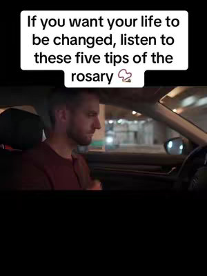 A man is driving a car, shown in a medium shot. White text on a black background is overlaid at the top of the image. The man is wearing a maroon shirt and focused on the road, with the city lights visible in the background.