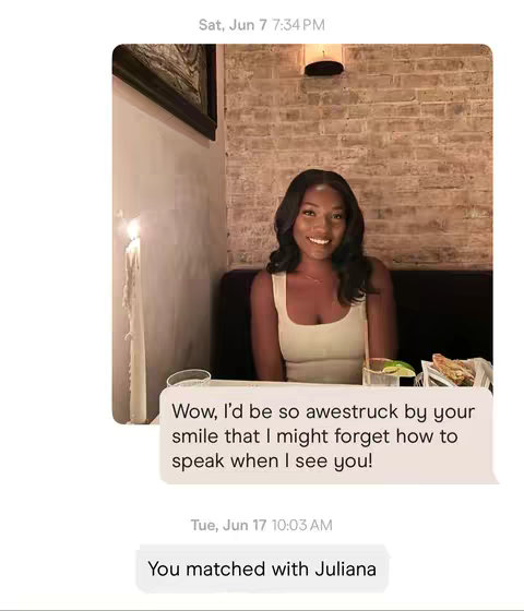 A screenshot of a dating app conversation. The background features a brick wall and a woman seated at a table, lit by a warm glow. The overlaid text is a message from a dating app. The message text is written inside a speech bubble with a date and time stamp.