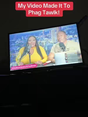 A TV screen displays a broadcast with two people, a woman in a yellow top and a man, each with microphones. Text in a red rectangular box is present above the screen.