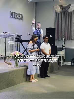 An image from a church service shows three individuals standing on a stage. A man in the center is raising his hand, presumably in prayer or teaching, while a woman and another man stand to his left and right respectively. The setting suggests a religious context, with a pulpit, flowers, and a banner that says "MIREN" in the background. The image has an overlay of text.