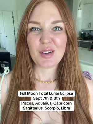 A woman with long auburn hair is centered in a selfie-style shot. She has fair skin, blue eyes, and is smiling slightly with her mouth open. She is wearing a gold necklace and a light-colored top. Behind her, a white kitchen is visible. Overlaid at the bottom, in a white rectangle, are black text lines stating: "Full Moon Total Lunar Eclipse Sept 7th & 8th Pisces, Aquarius, Capricorn Sagittarius, Scorpio, Libra".