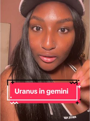 A selfie-style video cover featuring a woman with long, dark hair, a nose ring, wearing a black cap and a white top. The background is blurred with a pinkish hue. The video has a text overlay of "Uranus in gemini" in a red box.