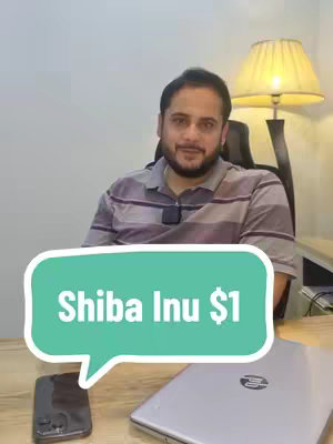 A man with a beard sits at a desk with a laptop and phone. A teal speech bubble overlay displays the text "Shiba Inu $1". A lamp with a beige lampshade is visible in the background.
