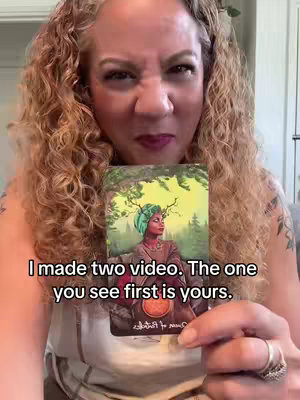 A woman with curly blonde hair is holding a tarot card in front of her face, making a displeased face. Text is overlaid on the image, and the setting appears to be indoors.
