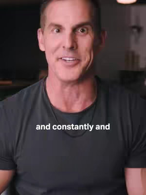 A medium shot captures a man from the chest up against a neutral background, he wears a dark gray t-shirt and is mid-speech, with a slightly open mouth and a direct gaze. The text overlayed adds context.