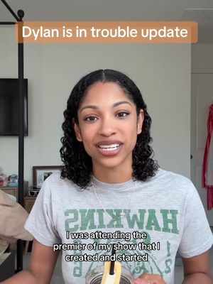 The cover image is a screen recording  of a woman speaking directly into the camera, which frames her from her chest to the top of her head in the center of the image. Text appears in a rectangular box at the top of screen. The woman's skin has a slight glow, suggesting natural or soft lighting. She has curly dark hair and is wearing a casual grey t-shirt with a green logo, most of which is cut off from view. The background is a soft white wall with a partial view of a dark curtain rod and a framed picture to the left and a red decorative item in the top right and lower right.