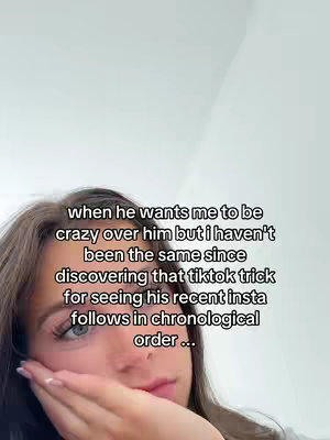 A close-up shot features a young woman with light skin and light brown hair, slightly out of focus. She gently touches her face with her right hand, index finger on her cheek, and her expression is one of subtle concern. The background is a plain, pale color, presumably a wall.