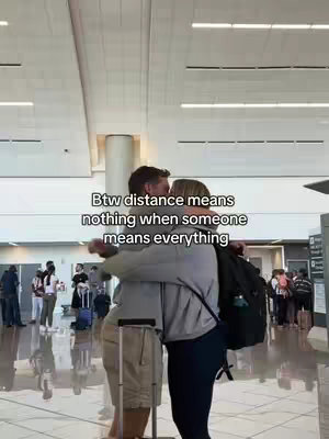 Two people embracing in an airport with text overlayed at the top. The image is brightly lit, showcasing the ceiling and background of the airport.