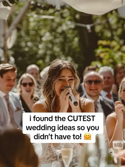 A woman at a wedding stands in front of a crowd with a microphone, mid-speech, appearing emotional. Text overlaid near the bottom reads 'i found the CUTEST wedding ideas so you didn't have to!'. Over her shoulder are other guests, blurred in the background, and the outdoor wedding setting includes greenery and dappled sunlight.