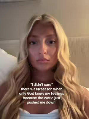 A selfie-style video with a young woman with long blonde hair looking directly at the camera. Text overlayed in the lower section of the screen includes a quote. The background is a plain, blurred interior space. The lighting appears natural, with soft shadows on her face.