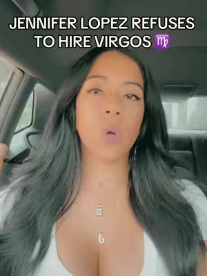 A selfie-style video showing a woman in the driver's seat of a car. The woman has dark hair and is looking directly at the camera with a slightly surprised or inquisitive expression. Text overlayed on the video reads 'Jennifer Lopez refuses to hire Virgos' with the Virgo symbol. She is wearing a white top, and there are visible car details behind her.