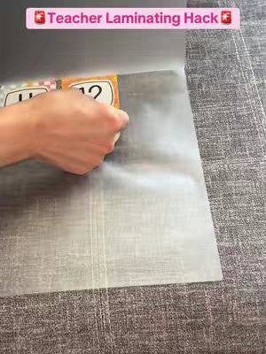 The cover image shows a hand placing a laminated card with the number "12" onto a transparent sheet, presumably part of a lamination process. Above, there is a pink rectangle with white text that reads "Teacher Laminating Hack."