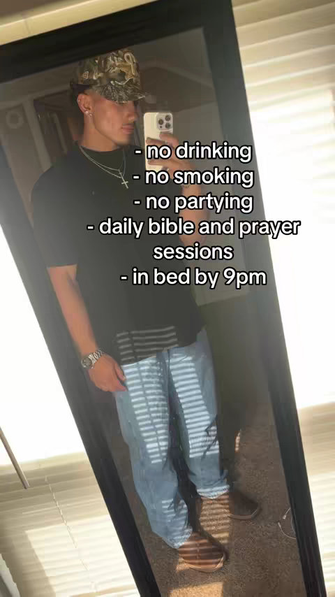 A young man is standing in front of a mirror, taking a selfie. He's wearing a camouflage hat, a black shirt, blue jeans, and brown boots. Text is overlaid in white listing rules like 'no drinking', 'no smoking', and other lifestyle choices.