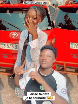 A selfie-style shot featuring two young people in front of two red vehicles. A young woman on the left is covering her mouth, while a young man on the right is smiling and pointing upwards. Text overlays add to the personal interaction, celebratory tone of the image.