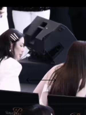 The cover image shows two women, possibly at a public event. One woman, on the left, is seen from the chest up, wearing a white top and has hair up with a hair pin. On the right side of the image, a woman is seen from behind, wearing a light-colored top and with long dark hair. The background is out of focus or dark and contains audio equipment.