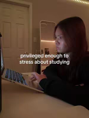 A young woman is shown in a dimly lit room, working on a laptop. The text overlay reads 'privileged enough to stress about studying.'