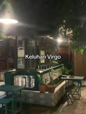 The image shows an outdoor cafe scene at night. The focus is on a seating arrangement with green tables and chairs, and some plants giving a natural touch. There are soft lights. Overall, the setting implies a relaxed, casual atmosphere.