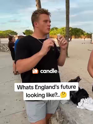A young man stands on a beach holding a small object, possibly food, talking to someone off-camera. The background features a beach with palm trees, a sidewalk, and other people. Overlayed text in a white box asks "Whats England's future looking like?.." with a thinking emoji.