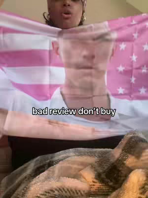 The image shows a person holding a pink and white flag with a faded American flag design. Behind the flag, a person's face is partially visible. The hook text 'bad review don't buy' appears at the bottom in a white font.