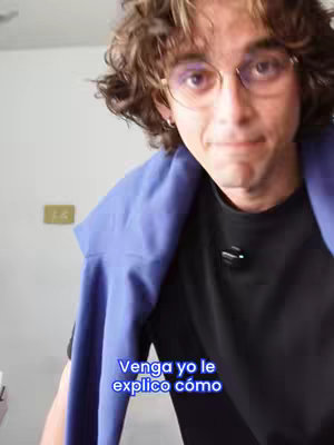 The cover image features a man with brown curly hair, glasses, and a black shirt. A blue garment is draped over his shoulders. Text overlayed in the bottom reads, "Venga yo le explico cómo". He is looking at the camera with a slightly concerned expression. The background appears to be a plain white wall.