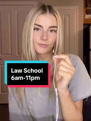 A young woman with blonde hair and a gray t-shirt stands in front of what appears to be wooden paneling, possibly a closet door. She has earphones and appears to be holding one of them up. A rectangular graphic in the bottom of the screen features the text 'Law School 6am-11pm'. The colors in the image are muted, featuring desaturated colors that create a casual aesthetic.