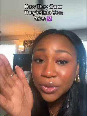 A woman with dark hair and a full face of makeup gestures toward the camera with her hand, while overlaid text reads 'How They Show They're Into You: Aries' and shows the Aries symbol.