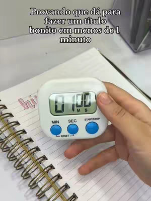 The image shows a digital timer on a notebook page, with the timer displaying a time of 1 minute. Above the timer is text in Portuguese that reads, testing that you can create a beautiful title in less than one minute. The notebook has a spiral binding, and a hand is holding the timer.