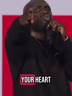 A man with a shaved head is holding a microphone and pointing towards the camera. Text overlayed says 'YOUR HEART' in a white font within a pink box. The man is wearing a black sweater, and the background has gradients of red and purple.