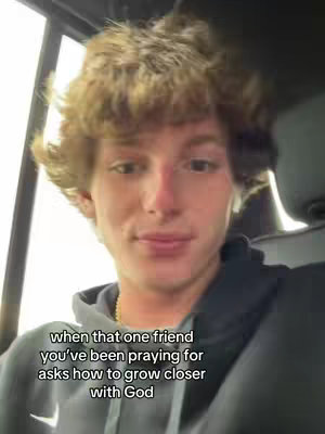 A selfie-style video featuring a young man with curly blonde hair, seated inside a vehicle. The man is facing the camera, and white text is overlaid on the bottom of the image. The background is slightly blurred, suggesting the inside of a car.