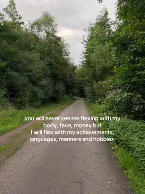 A path winds through a dense forest with towering trees and lush greenery on either side. The sky is overcast, providing soft lighting. Text overlayed on the image reads a motivational quote about what the creator chooses to 'flex'.