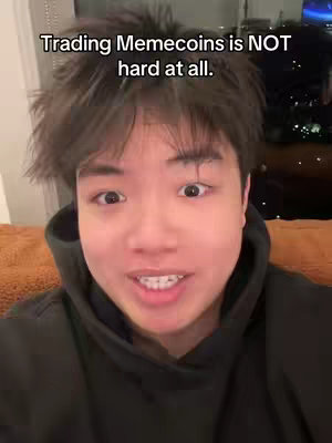 A selfie-style shot of a young man with short dark hair and expressive eyes. He is centered in the frame, wearing a black hoodie, and speaking toward the camera. The background is blurred, suggesting a cozy indoor setting.