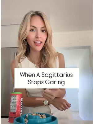 A young woman with blonde hair smiles and gestures with her hand while standing in a kitchen setting. A text overlay reads, "When A Sagittarius Stops Caring." Behind her is a refrigerator and a counter with a can of soda on it. In the foreground, a blue bowl with what appears to be dog food is visible.