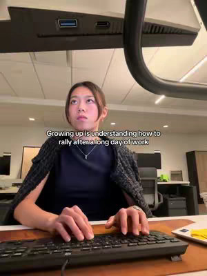 A woman is shown seated at a desk, typing on a keyboard. Her face is visible, and she's looking up and to the left thoughtfully. The image has text overlay. The lighting is diffused, suggesting an office setting.