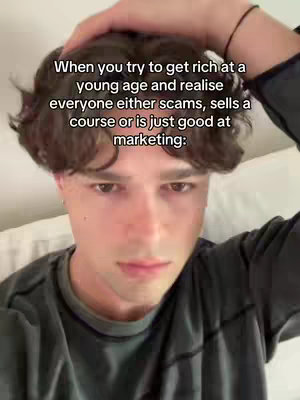 A selfie-style video cover. A young man with dark curly hair and a concerned expression is centered in the frame. His right hand is placed near the top of his head. Text overlayed on the image reads, 'When you try to get rich at a young age and realise everyone either scams, sells a course or is just good at marketing:' The background is blurred.
