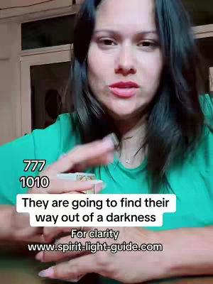 A woman with long dark hair and a green top is centered in the frame, holding a rolled object in one hand. Text overlays at the bottom of the frame: a text box with the words "They are going to find their way out of a darkness" and underneath it "For clarity www.spirit-light-guide.com". Numbers "777" and "1010" are stacked on the left side of the frame.