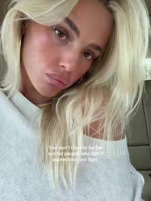 The cover image is a close-up selfie of a woman with blonde hair, looking towards the camera with a slight downward gaze. Her features display a subtle blush, and she wears small gold hoop earrings. The background is slightly blurred, suggesting an interior setting, and a text overlay with the quote is positioned below her face.
