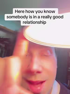 The cover image is a selfie-style shot featuring a man looking towards the camera. Above him, a text overlay indicates the video is related to relationships focusing on a good relationship. The lighting seems to be from an overhead source, casting shadows and creating a warm, slightly overexposed effect. The man is touching his face and smiling, suggesting a positive and friendly demeanor. The background appears to be a dimly lit interior, possibly a room, without clear details.