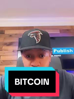 The image features a man wearing a black baseball cap with an Atlanta Falcons logo. He is positioned in front of a wooden-paneled wall and a screen with text. A rectangular banner at the bottom displays the word 'BITCOIN' in white letters against a teal and red background. The man is focused directly into the camera with a serious expression.