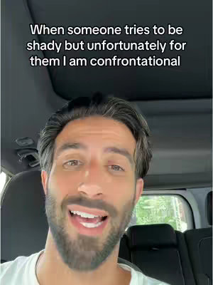 A man with a beard and short dark hair is seated in the driver's seat of a car and speaking towards the camera. Text overlayed on the top says, "When someone tries to be shady but unfortunately for them I am confrontational."