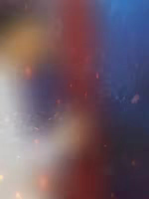 An abstract image composed of blended colors: primarily deep blue and red hues, with accents of yellow and white. The colors merge and transition smoothly, creating a blurred effect with small, glowing particles scattered throughout the image.