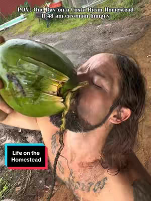 A man is pouring a green liquid from an opened large fruit, like a coconut, into his mouth. The image is taken from a POV perspective, with the man's face and a portion of his upper body visible. Text overlays at the top and bottom indicate the scene's context as a Costa Rican homestead with the time.